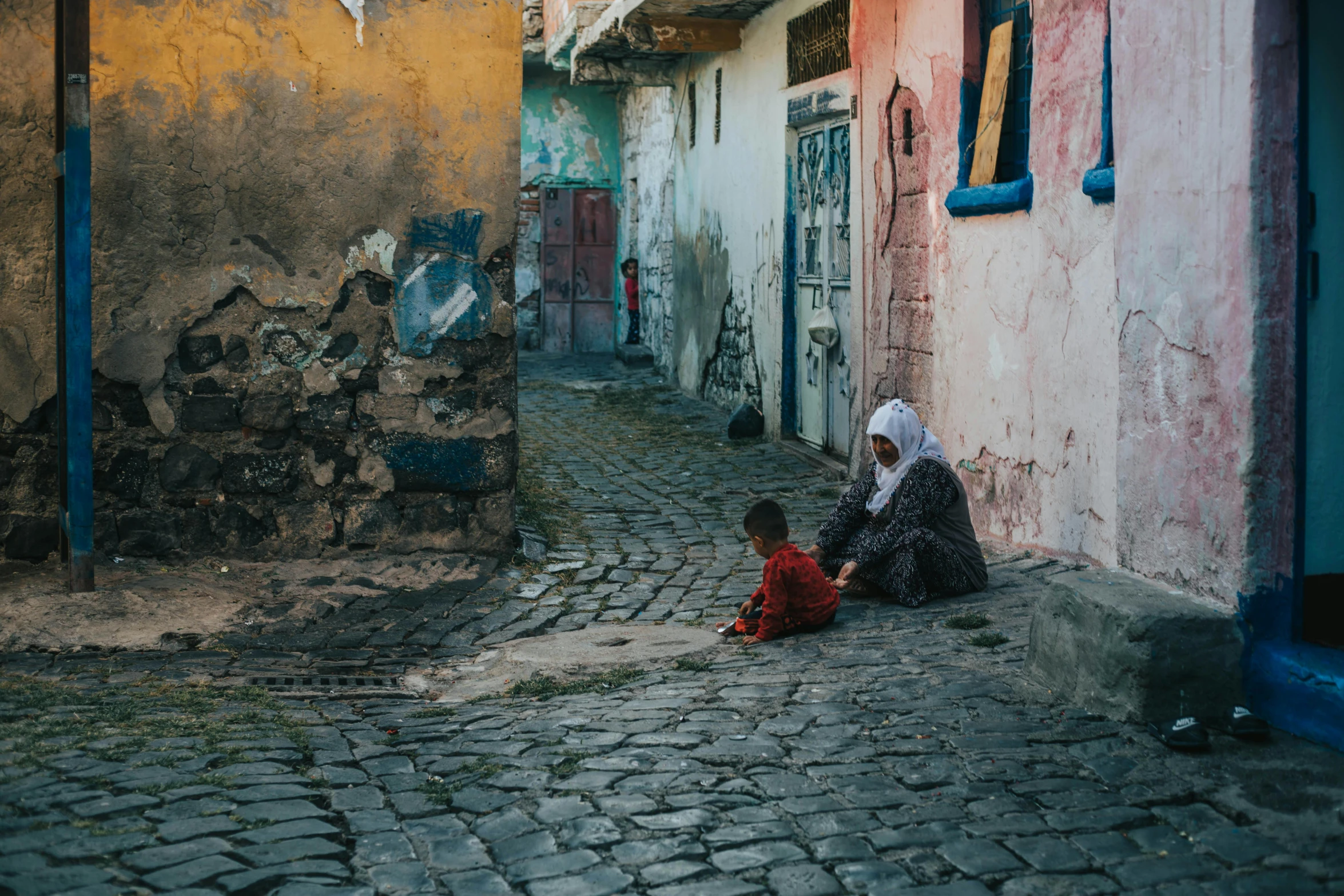 two people are sitting outside on the ground near buildings