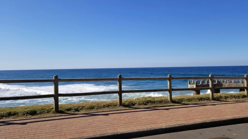 the boardwalk overlooks the blue ocean with wooden benches on it