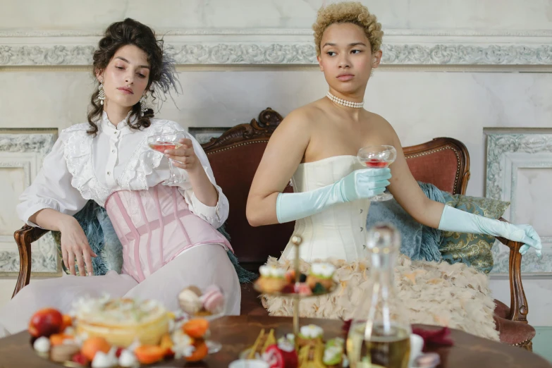 two women wearing white dresses sitting in an ornate chair