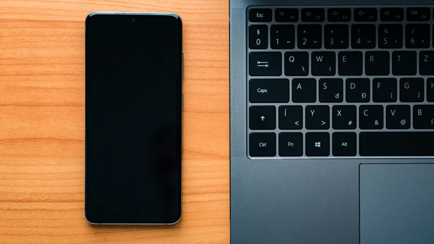 a cell phone, laptop and keyboard on a desk