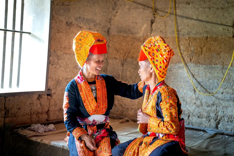 two women wearing brightly colored clothing, one in orange and the other in red, share a conversation