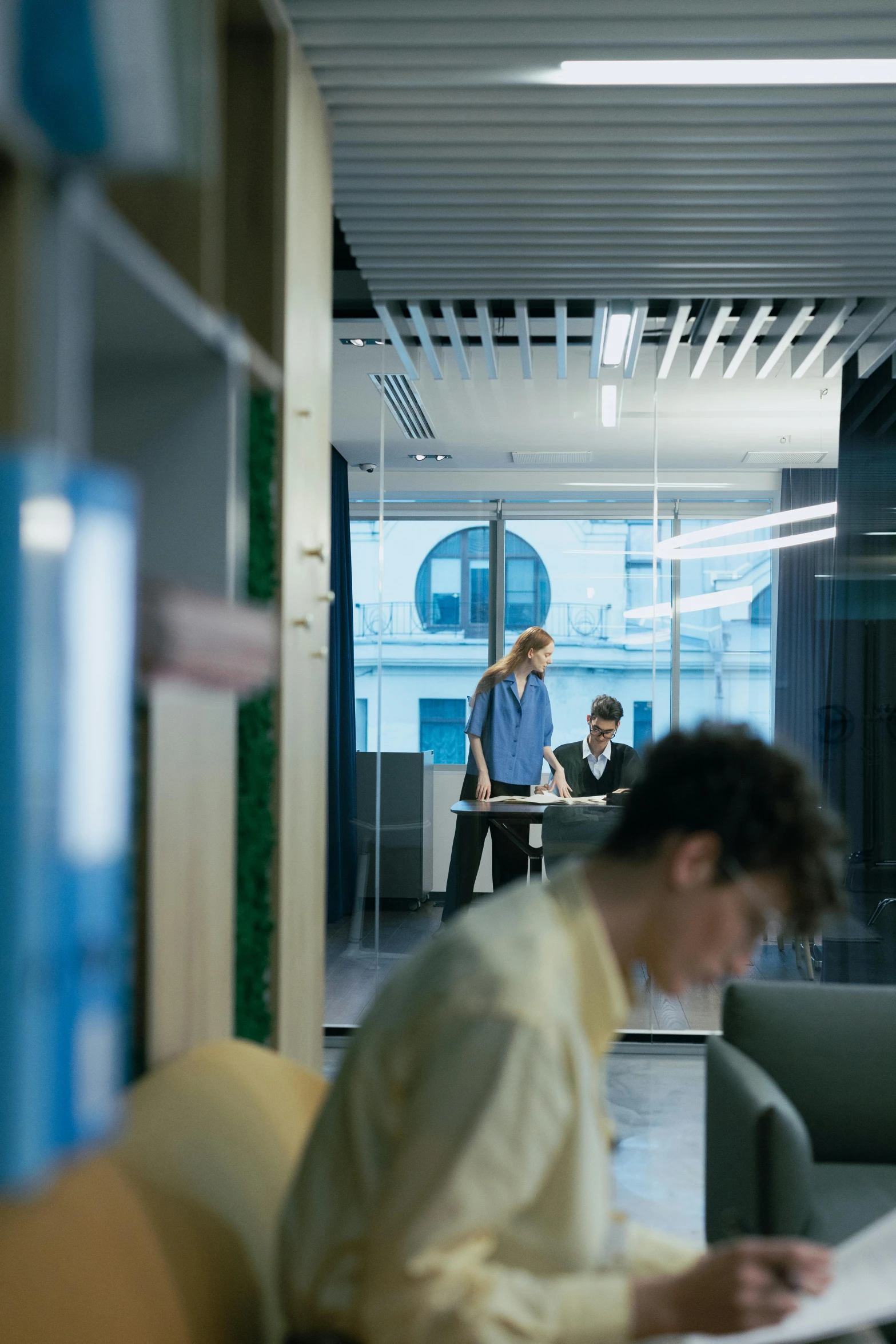 there is a woman working at the desk and a man walking by