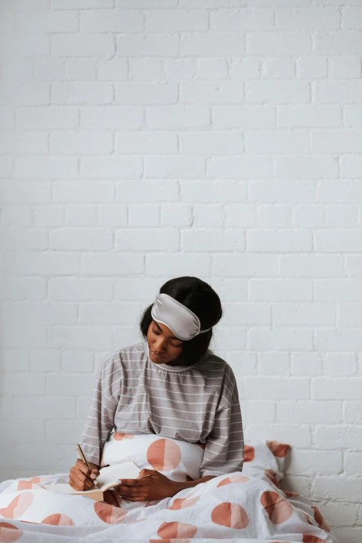 a woman sitting on a bed writing with a pen