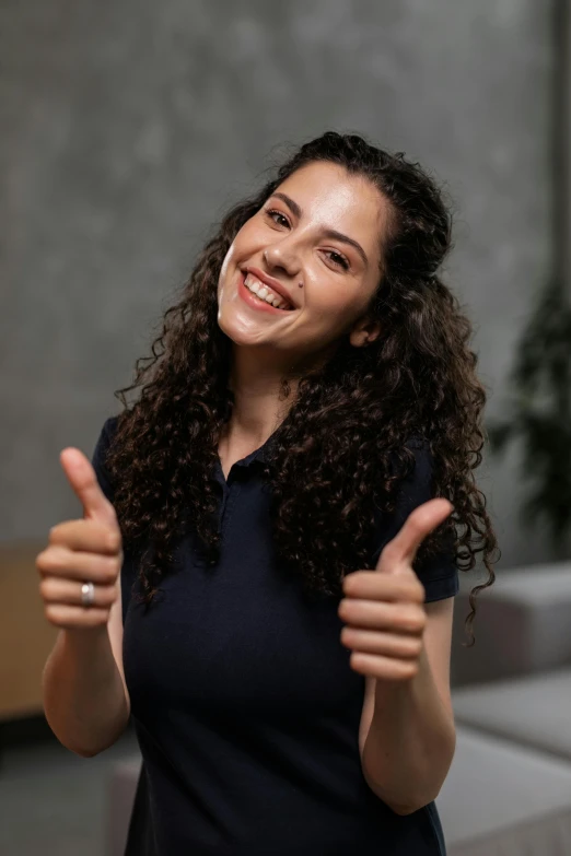 a woman with curly hair and a smile gives the thumbs up sign