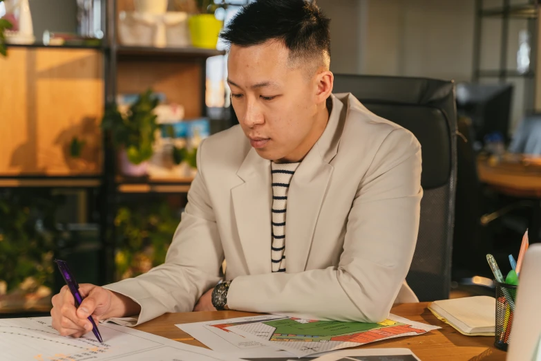 an asian man at a desk writing soing on paper