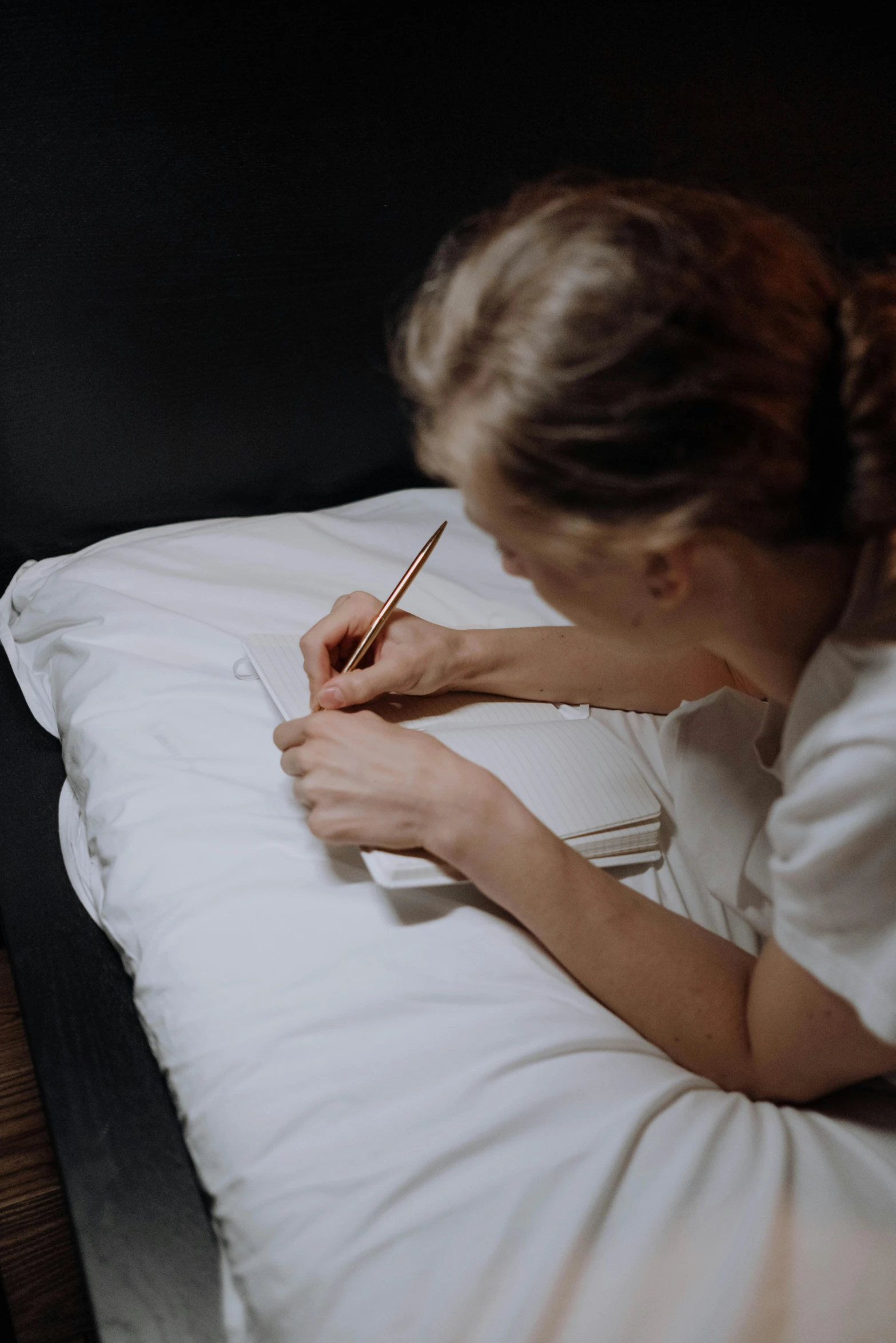 a woman writing on a bed with her hand resting on a pillow