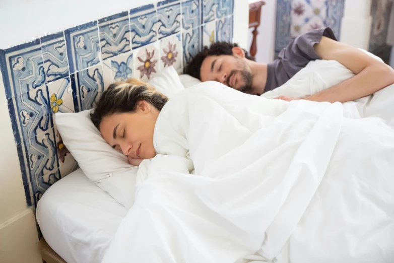 the couple is sleeping in bed with white sheets