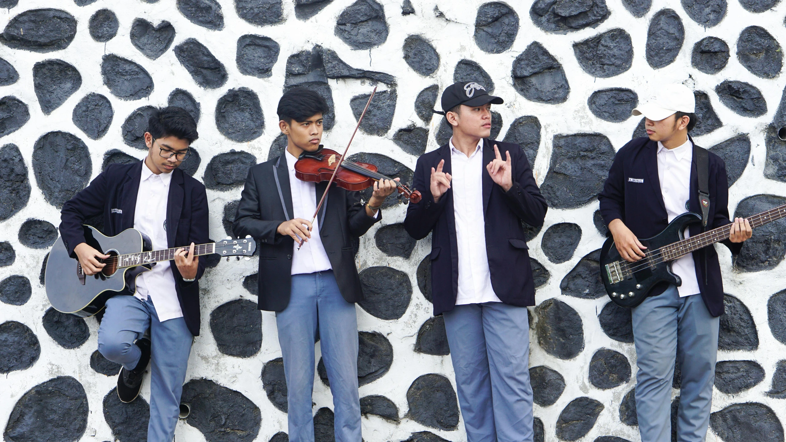 young men playing musical instruments against a rock wall