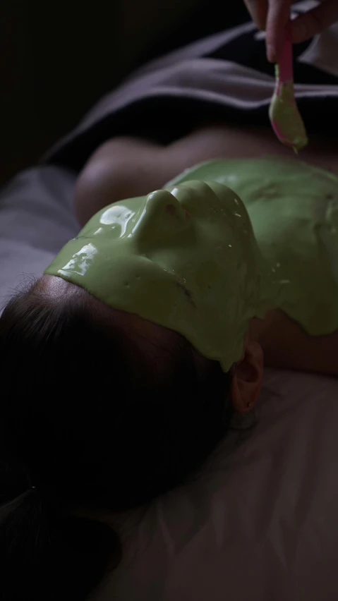 a  getting her face covered in bright green paste