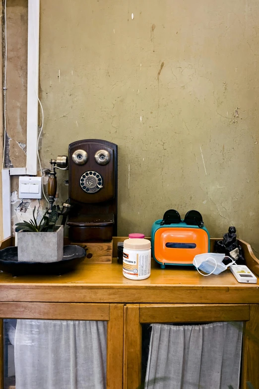 a dresser with a small coffee maker, vase, mug and curtain