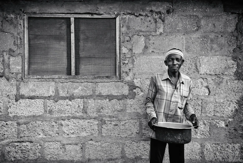 a man standing against a brick wall with a bucket in front of him