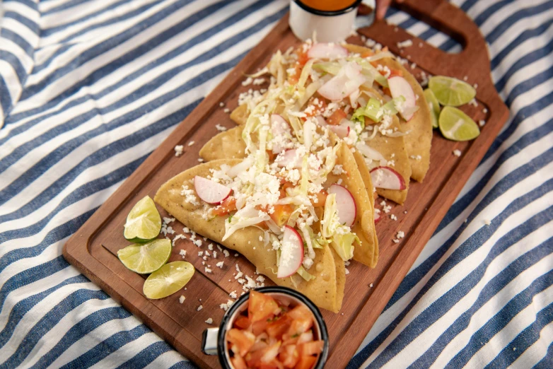 a wooden  board topped with tacos next to a bowl of salad