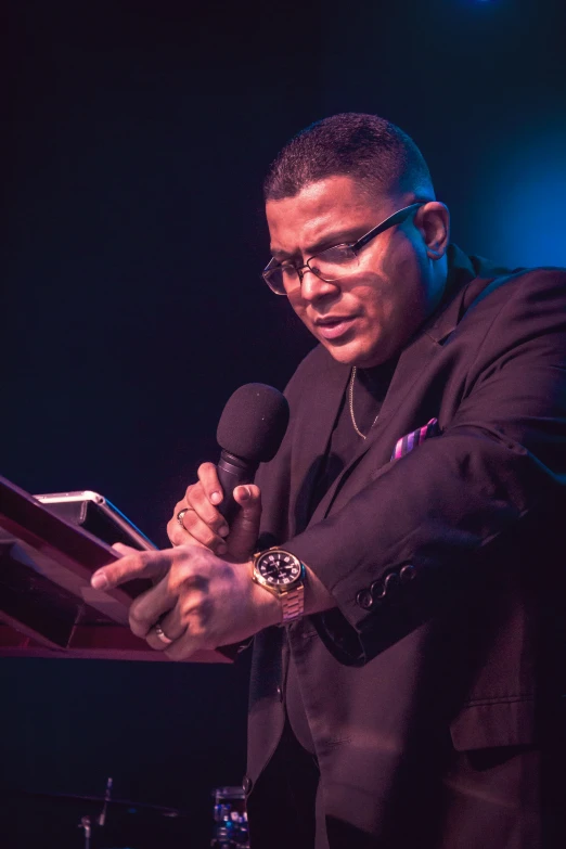 a man in black suit holding a microphone in front of a laptop