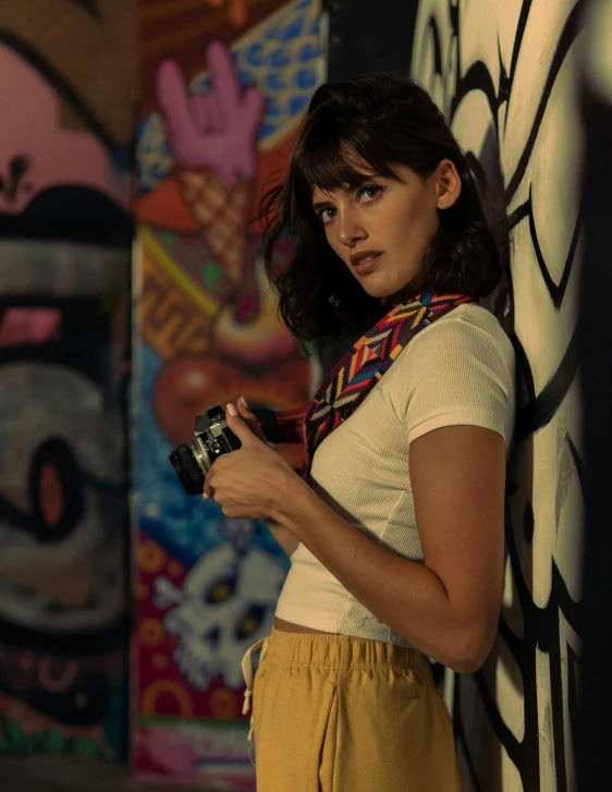 girl standing against the wall, using a camera and a large mural