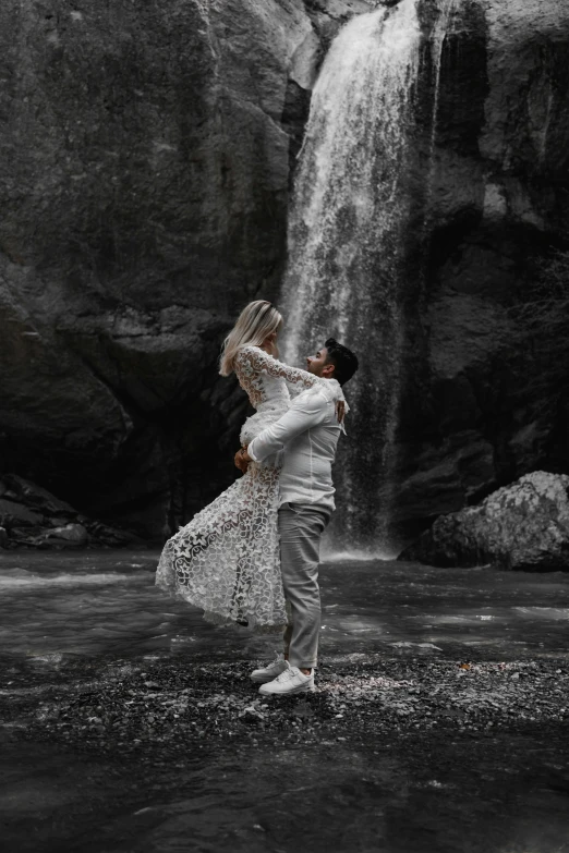 a couple standing in the water next to a waterfall