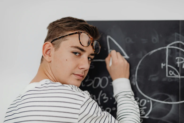 a boy in striped shirt and glasses is writing on a blackboard