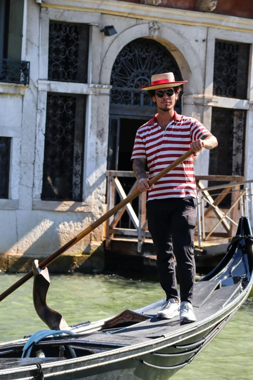 a man standing on top of a gondola on a canal