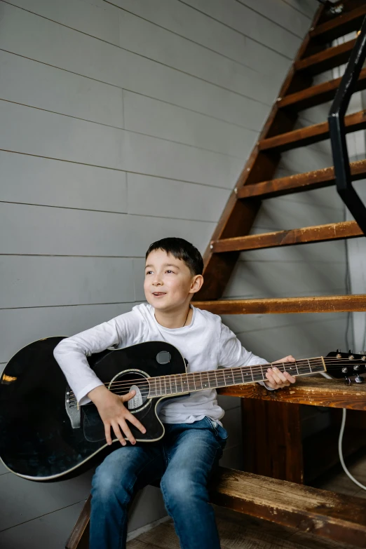 the boy is sitting with an acoustic guitar on his lap