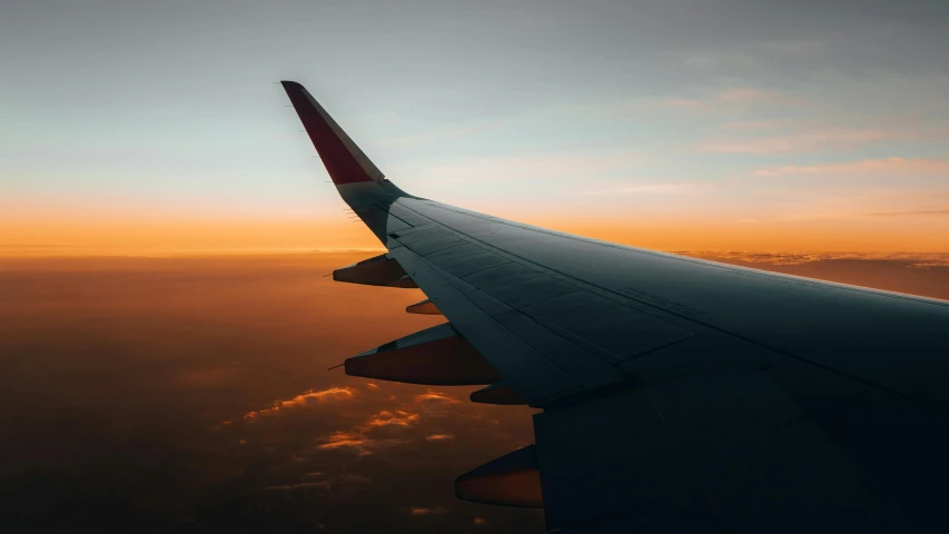 the wing of an airplane above the clouds during sunset