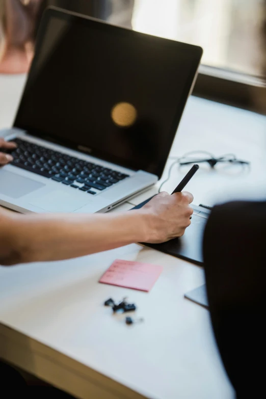 a laptop on a desk with two hands writing