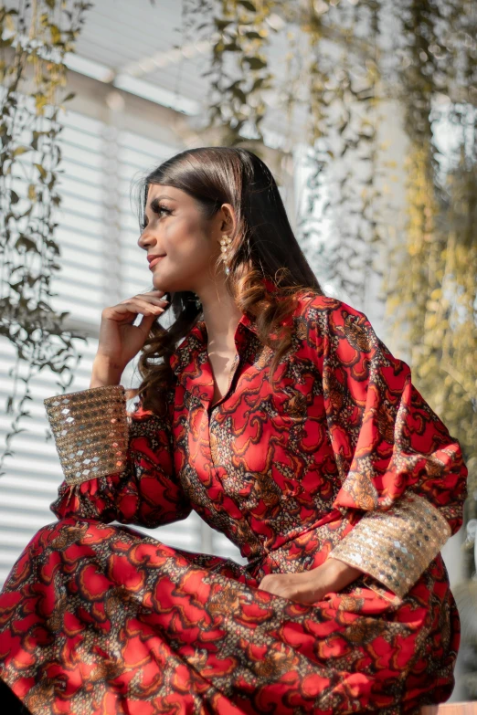 a young woman sitting on the ground while wearing a red and gold dress