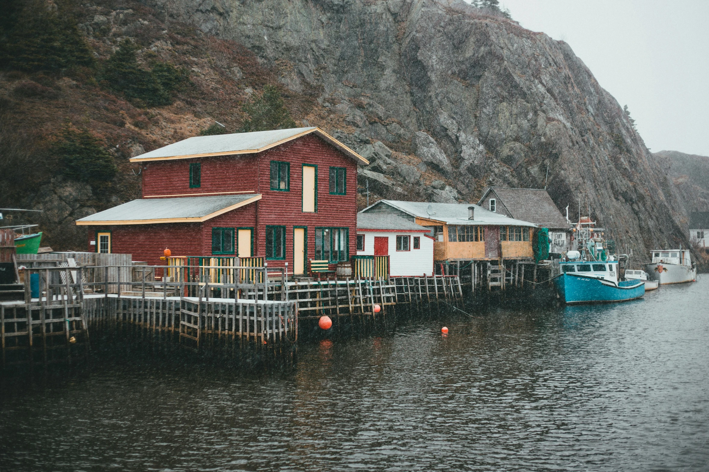 boats and a red house on the water near a mountain