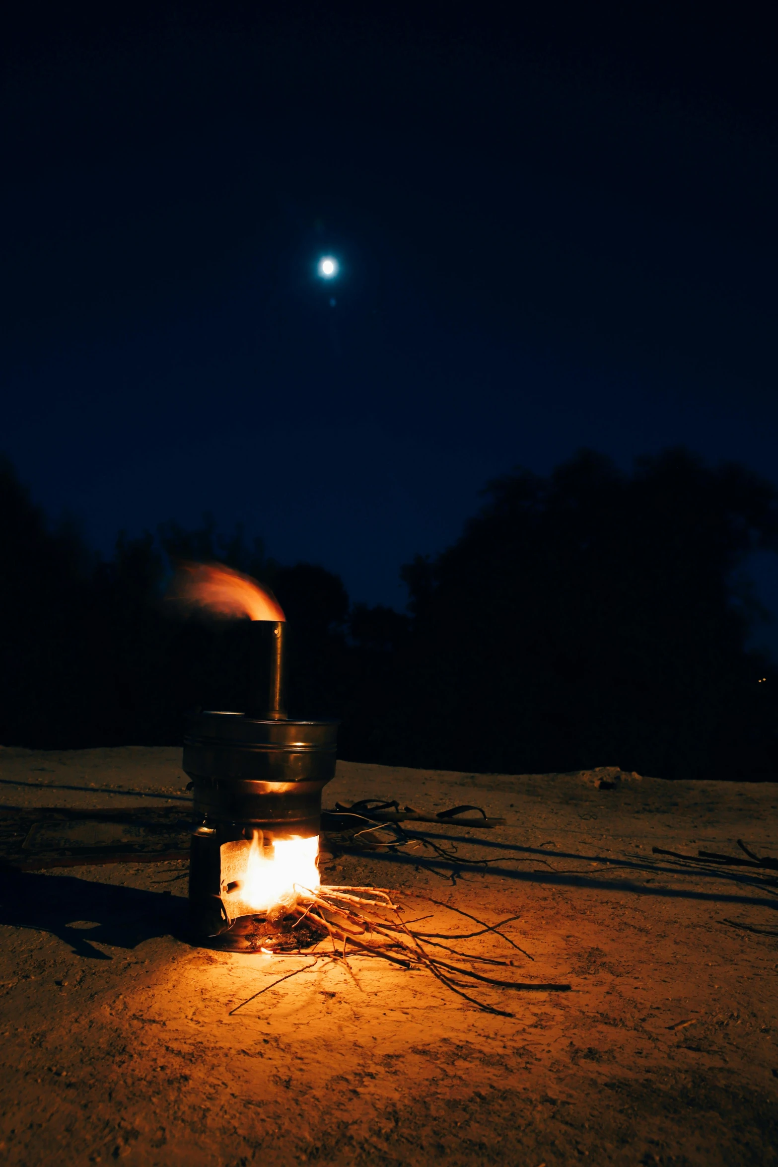 a person sitting next to an open fire with a full moon