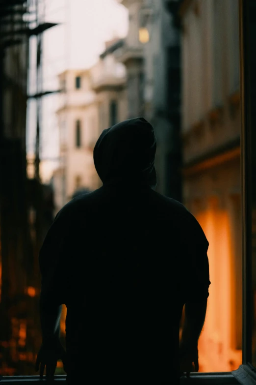 a person wearing a hooded coat looks out a window