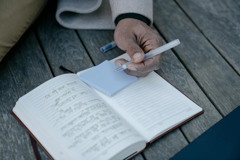 person holding pen and writing on notebook on wooden deck