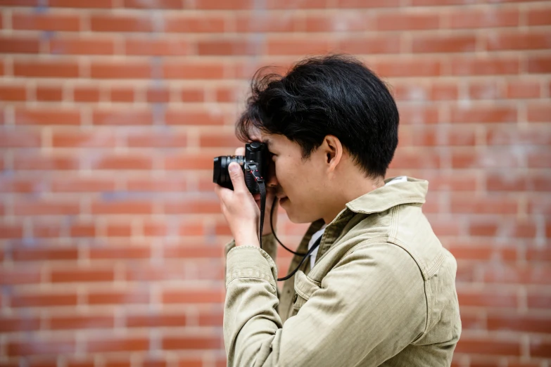 man taking pos with his cell phone by a brick wall