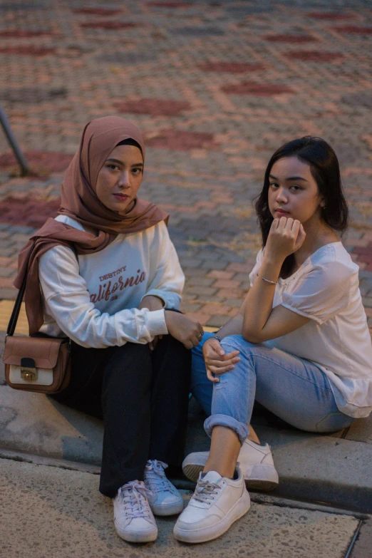 two women are sitting on the sidewalk one holding a hand bag