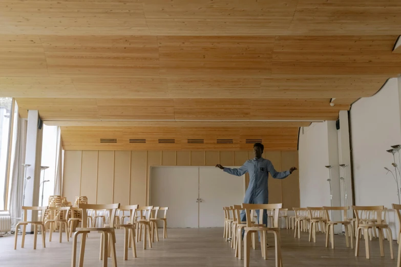 a man stands near a row of chairs as he holds his hands open