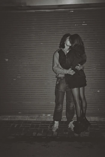 a couple hugs near a garage door while kissing