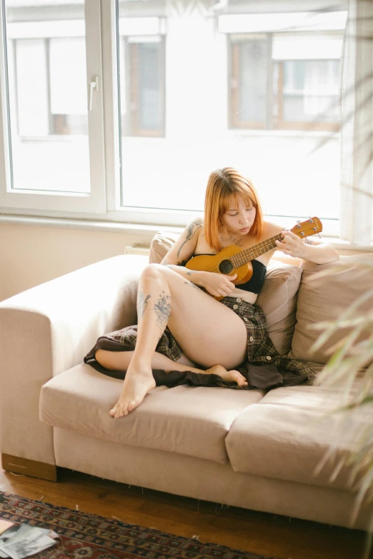 a woman with a tattoo plays the guitar on the couch