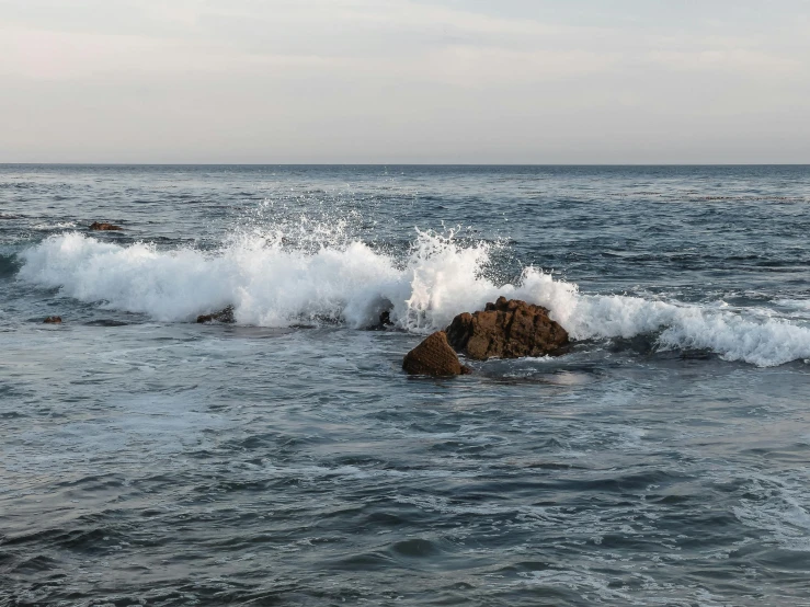 an ocean wave crashes over a rock in the water