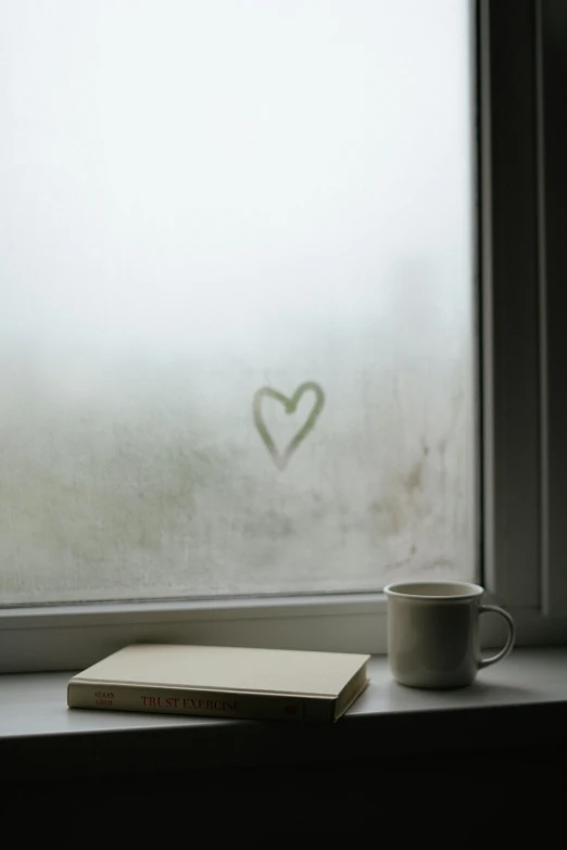 book and coffee cup sitting by window in rain storm