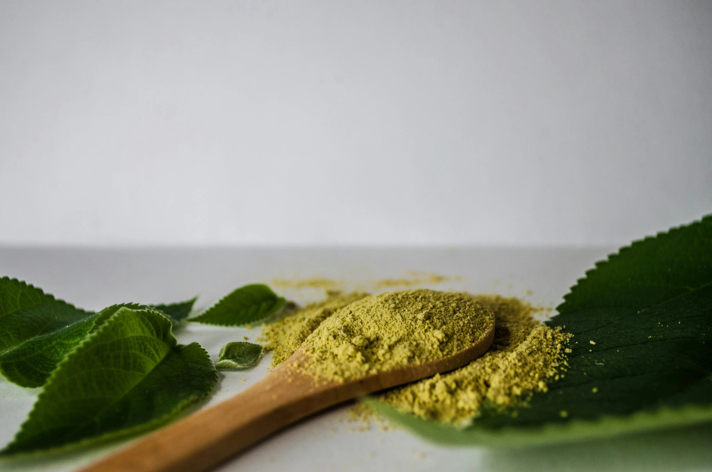 a green powder and wooden spoon next to leafy greens