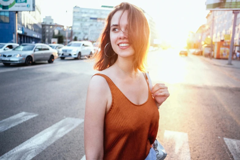 an attractive woman in a brown tank top crosses a city street
