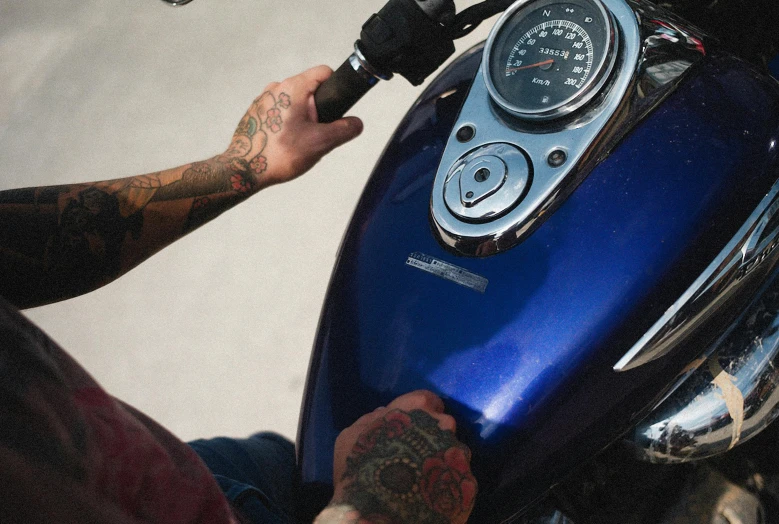 man with tattograph showing his tattoo on arm sitting down on a motorcycle