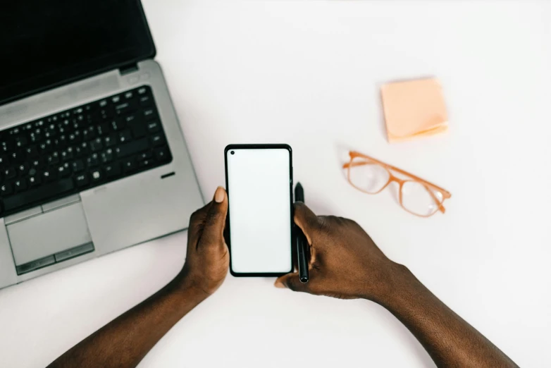 someone holding up an iphone next to a laptop