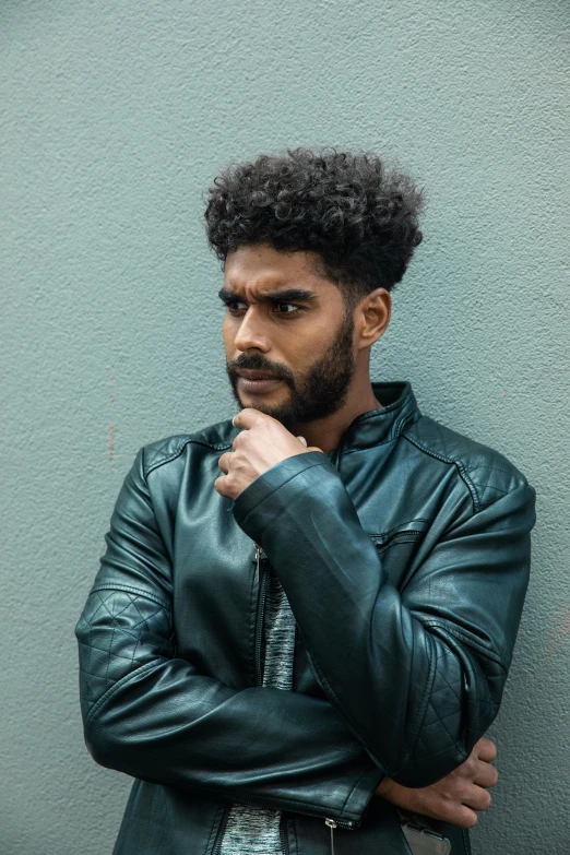 a man standing and posing against a wall with his hand on his cheek