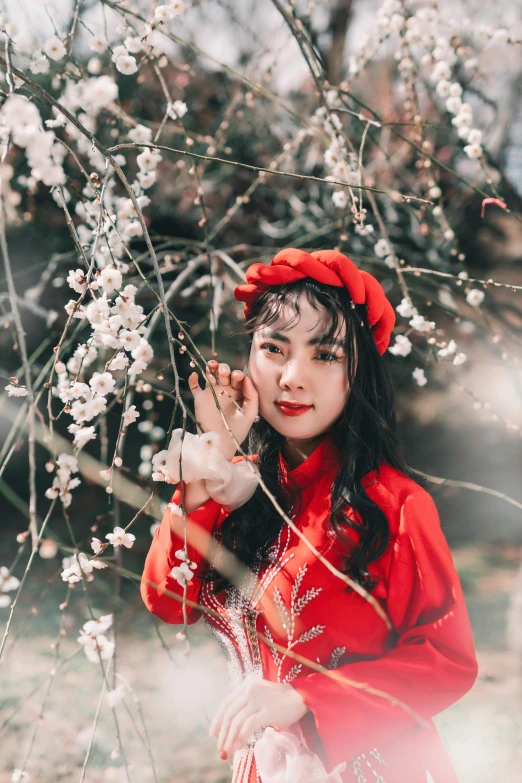 an asian woman in red poses in front of a blooming tree