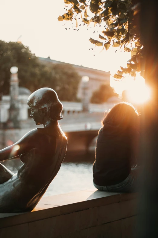 two people sitting on the ledge in front of a body of water