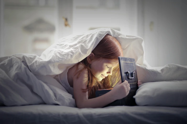 a girl lying in bed with a camera under her blanket