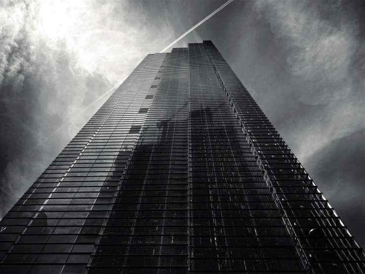 an upward view of the top of a skyscr under a cloudy sky