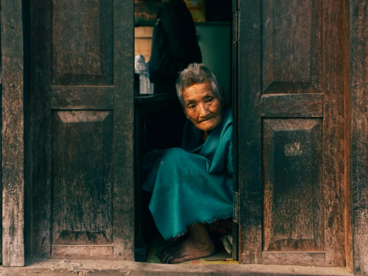 an old woman with blue scarves and sitting outside of an open door