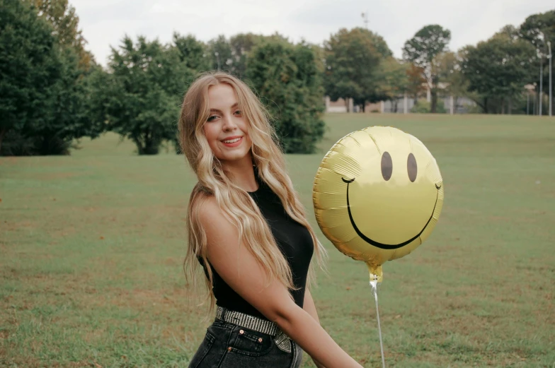 a young woman is posing with her balloon in the shape of a smiling face