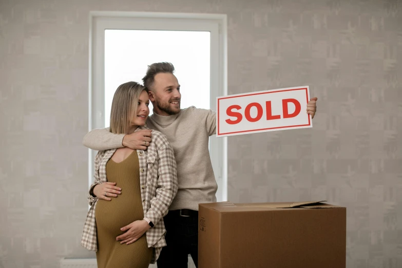 a man and woman pose for a pograph holding a realtor sign