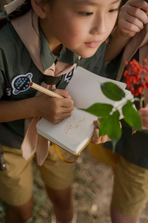 two girls writing in a notebook by a tree