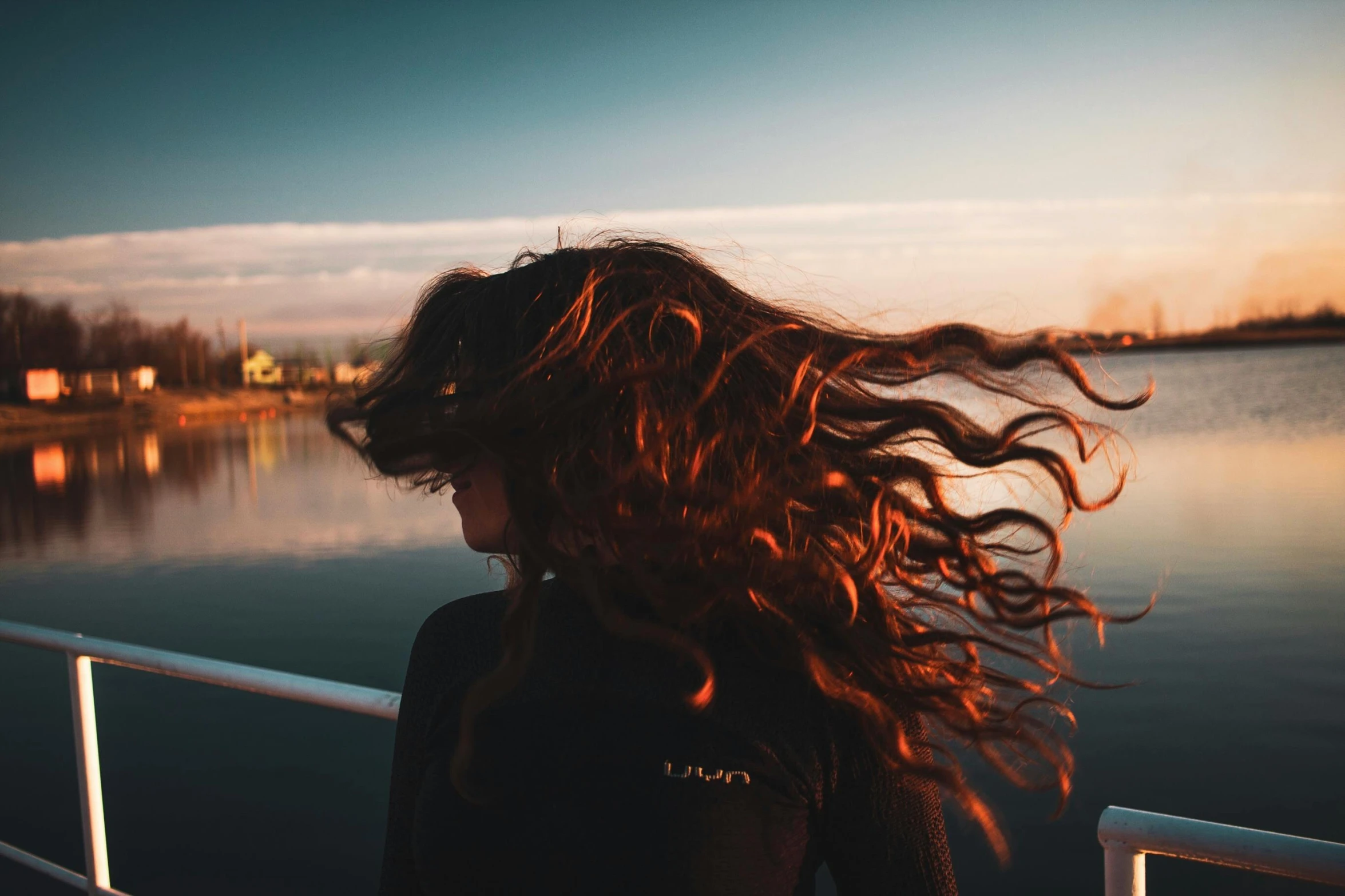 woman with large, long, flowing hair looking across a railing at the river